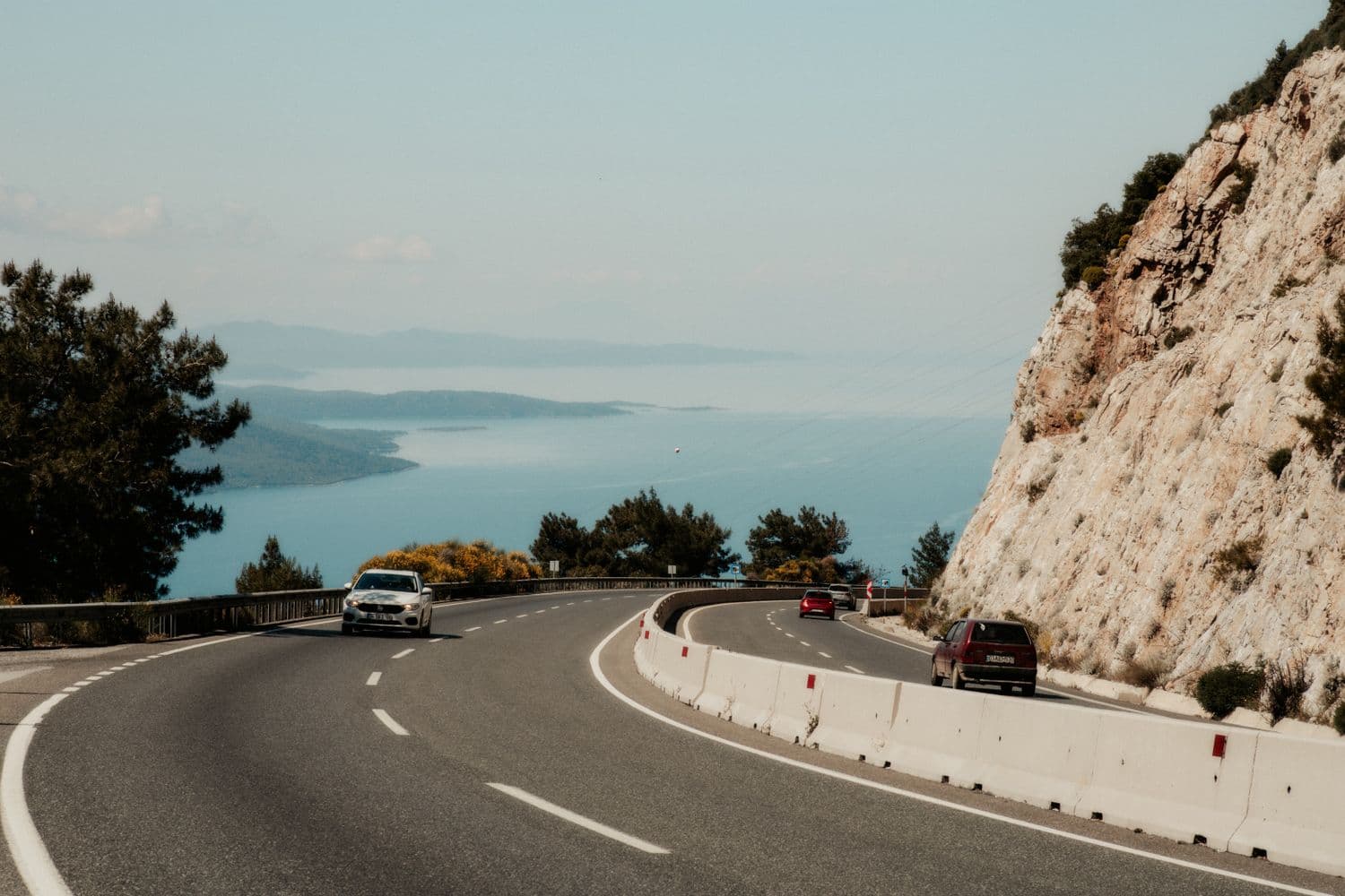 Cars driving along a sunlit coastal road above the Adriatic sea